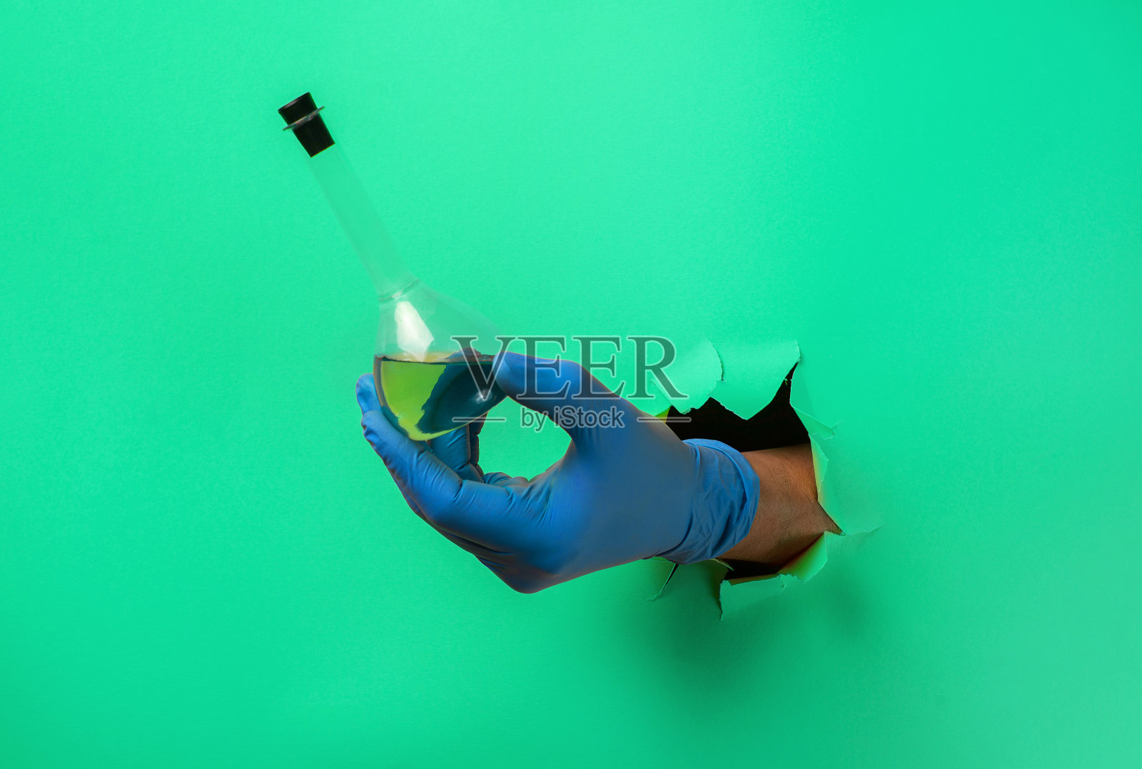 科学家手持有实验室玻璃器皿的烧瓶，穿过纸上的破洞照片摄影图片