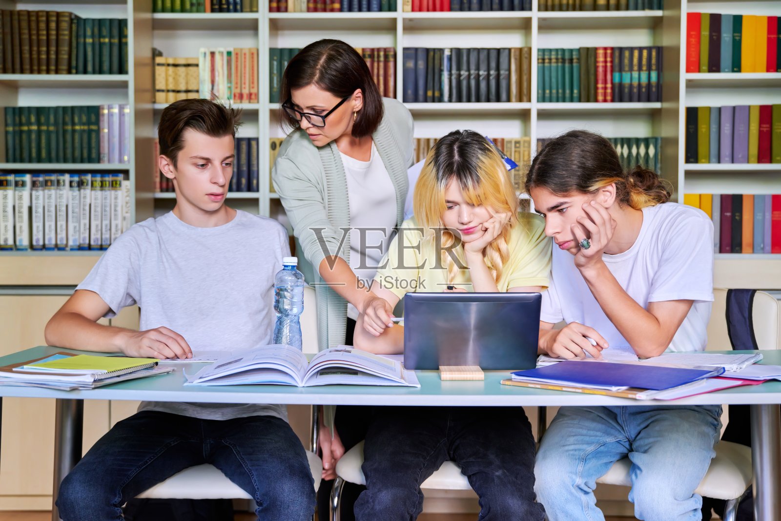 一群十几岁的学生在女老师的指导下在图书馆课上学习照片摄影图片