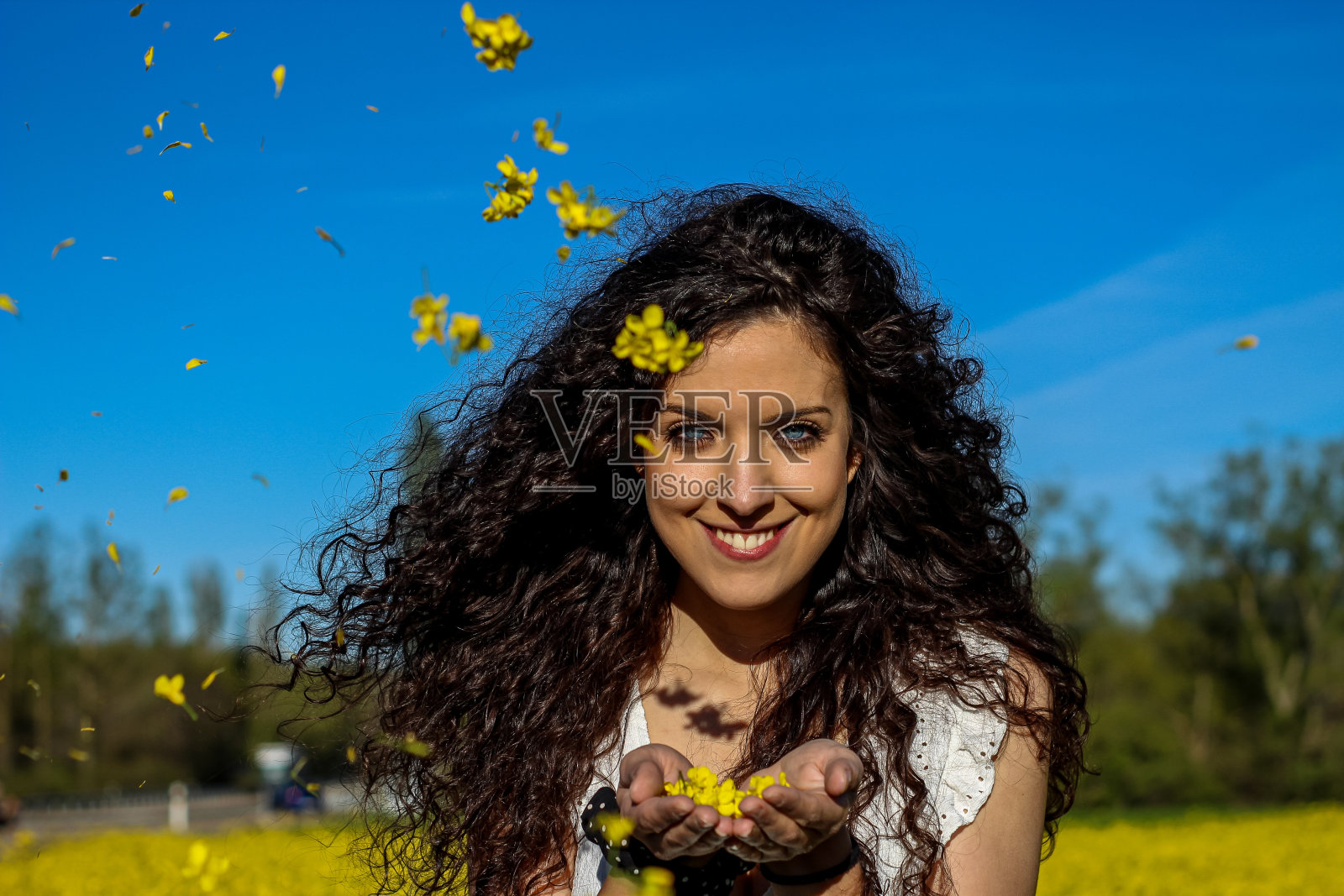 一个美丽的年轻女子的肖像微笑着看着相机，黄色的花瓣在她的手中照片摄影图片