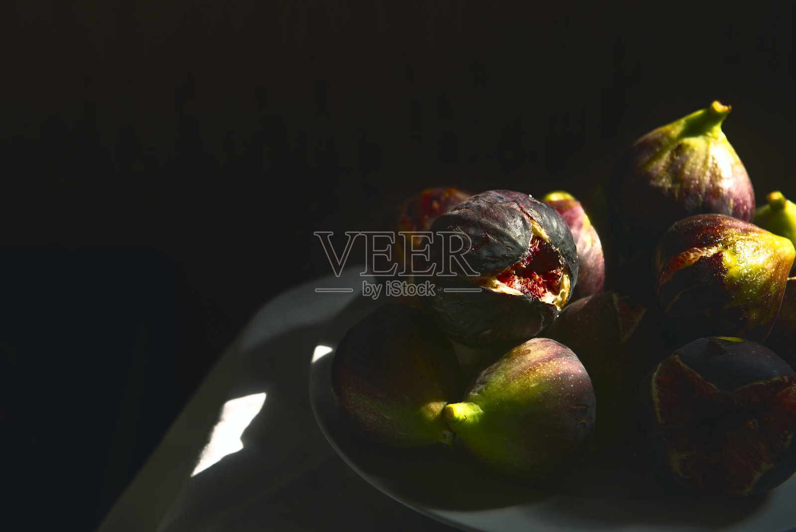 新鲜的无花果。这张照片很低调。阳光照射在桌子上成熟的无花果上。成熟芬芳的无花果，半开着。复制空间，特写，软选择焦点。紫色的阴影。艺术的观点照片摄影图片