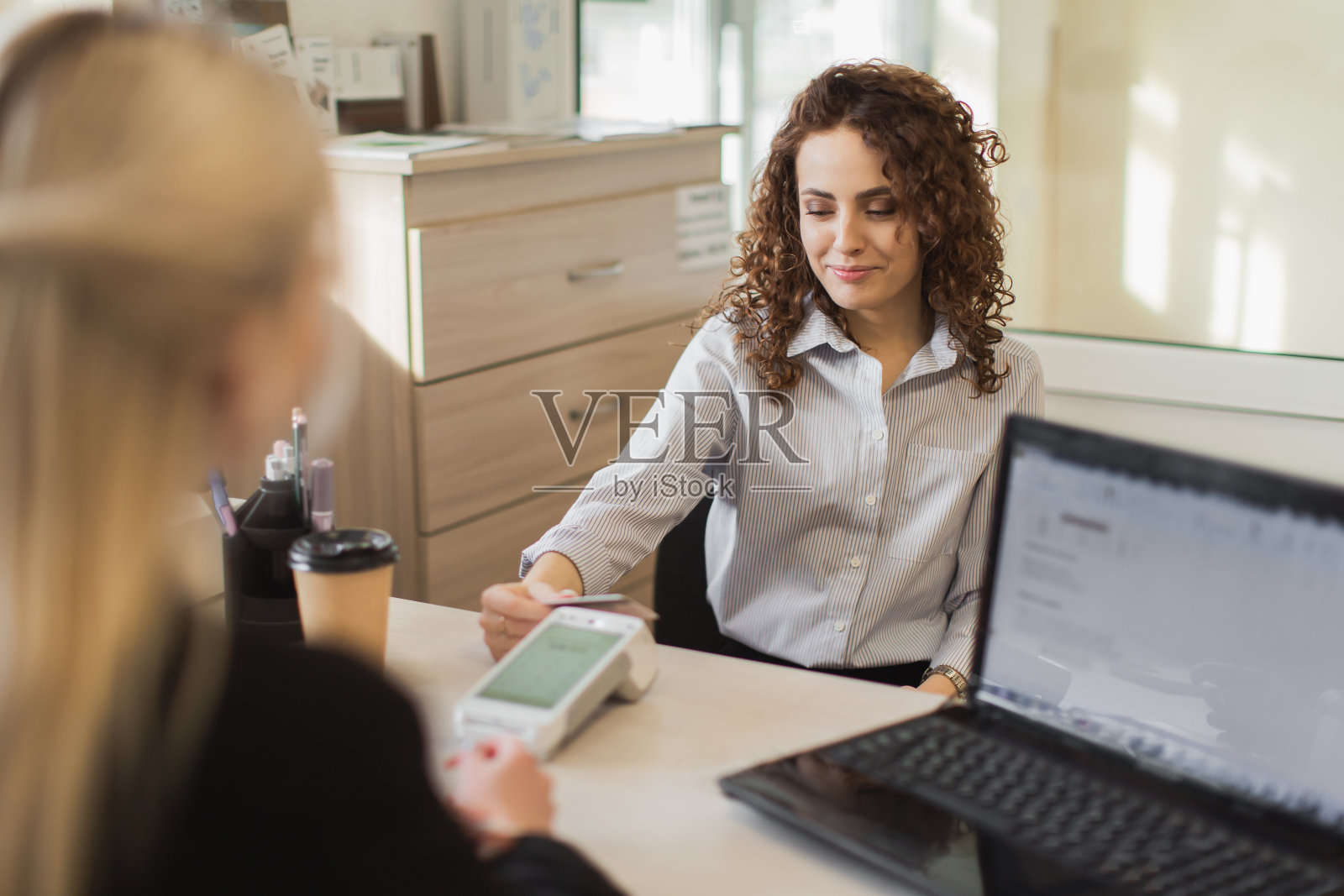 零售支付。年轻女子在家具店用信用卡付款。餐桌上的收银员为顾客服务。零售购买。小生意。事务处理。买家在商店照片摄影图片