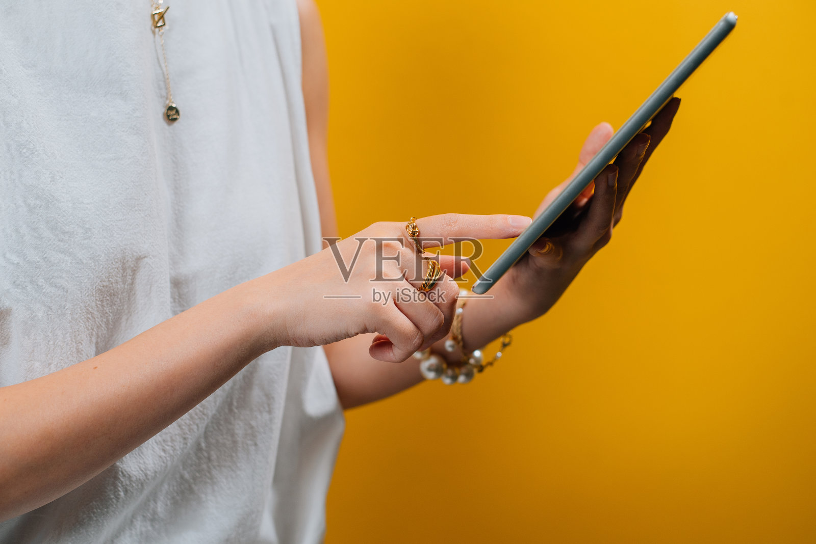 女性使用数码平板电脑的特写镜头，配以金戒指、珍珠手链等奢侈配饰照片摄影图片