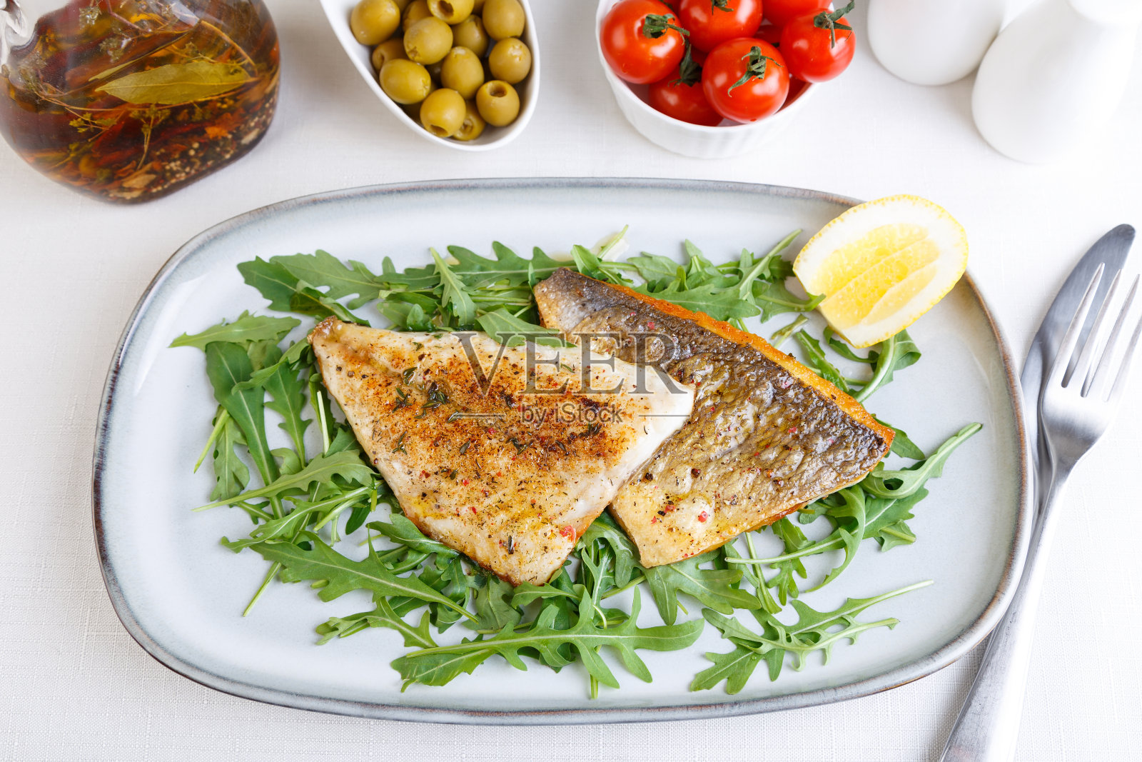 油炸鱼柳脆皮。芝麻菜，圣女果，橄榄，柠檬和橄榄油。传统的地中海菜。白色照片摄影图片