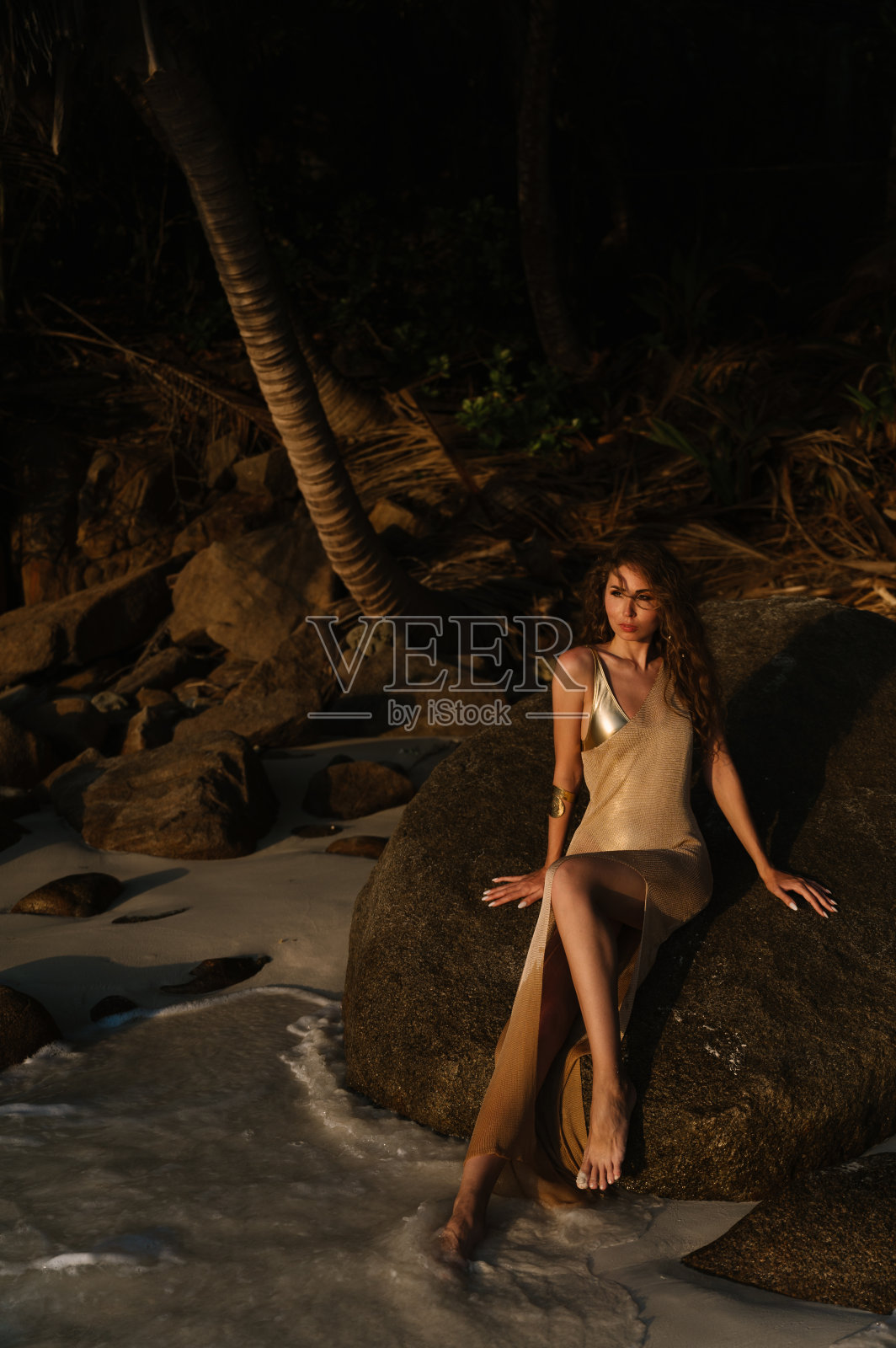 美丽的年轻女子在塞舌尔的马埃岛或拉迪格岛的日落海滩上，穿着长长的金色连衣裙，有“第二皮肤”的效果照片摄影图片