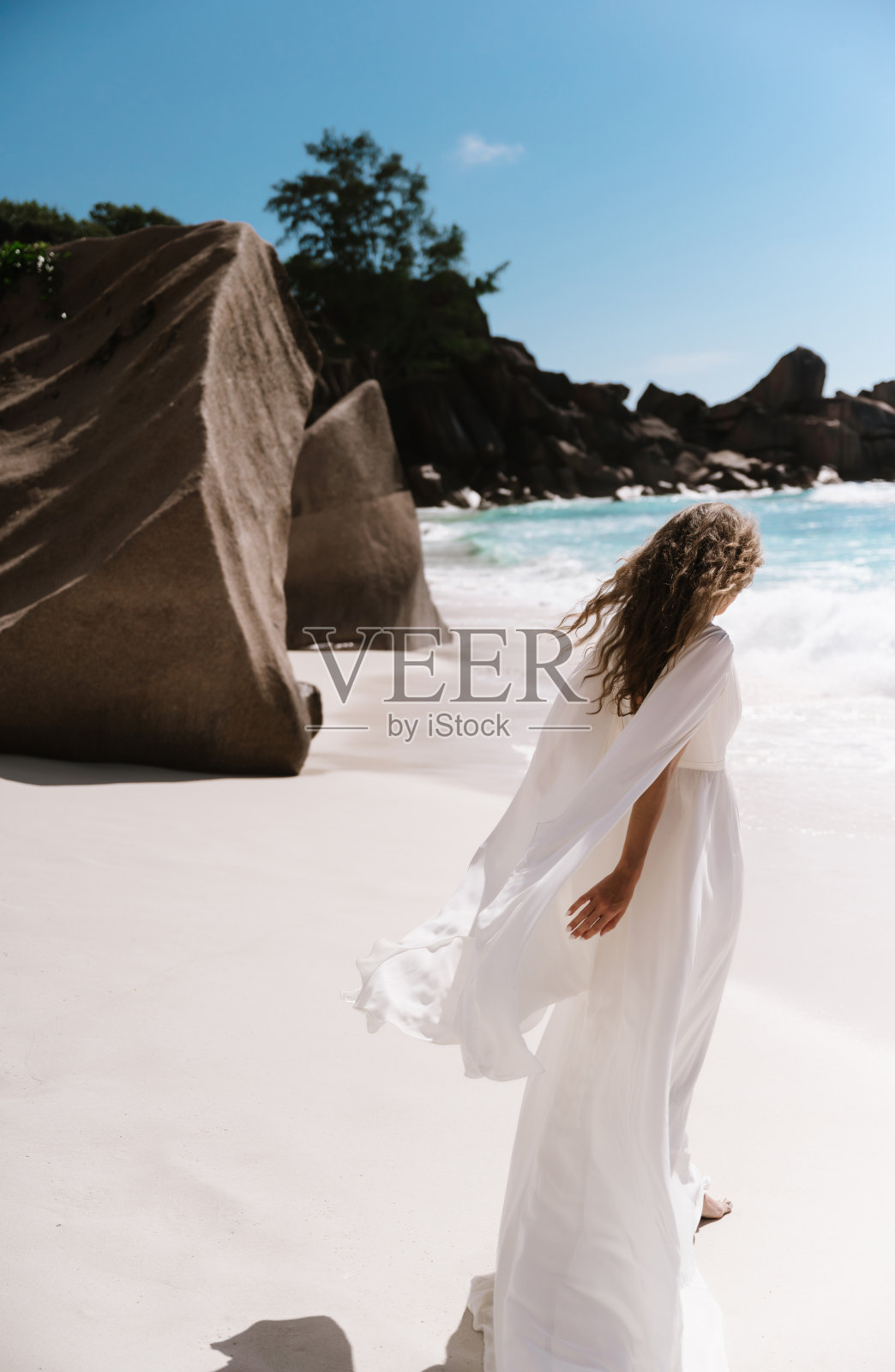 美丽的年轻女子新娘在塞舌尔的马埃岛或拉迪格岛的海滩上穿着长长的白色婚纱照片摄影图片