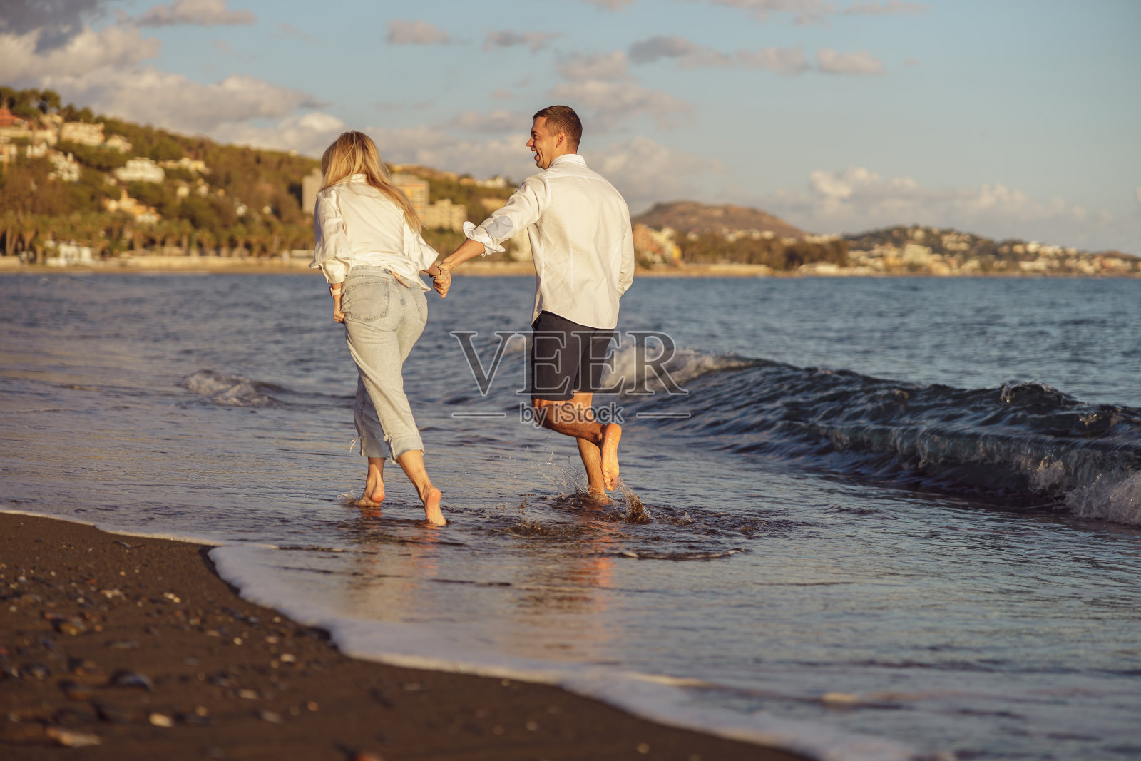 夕阳西下，一对幸福的夫妇在海边奔跑的背影照片摄影图片