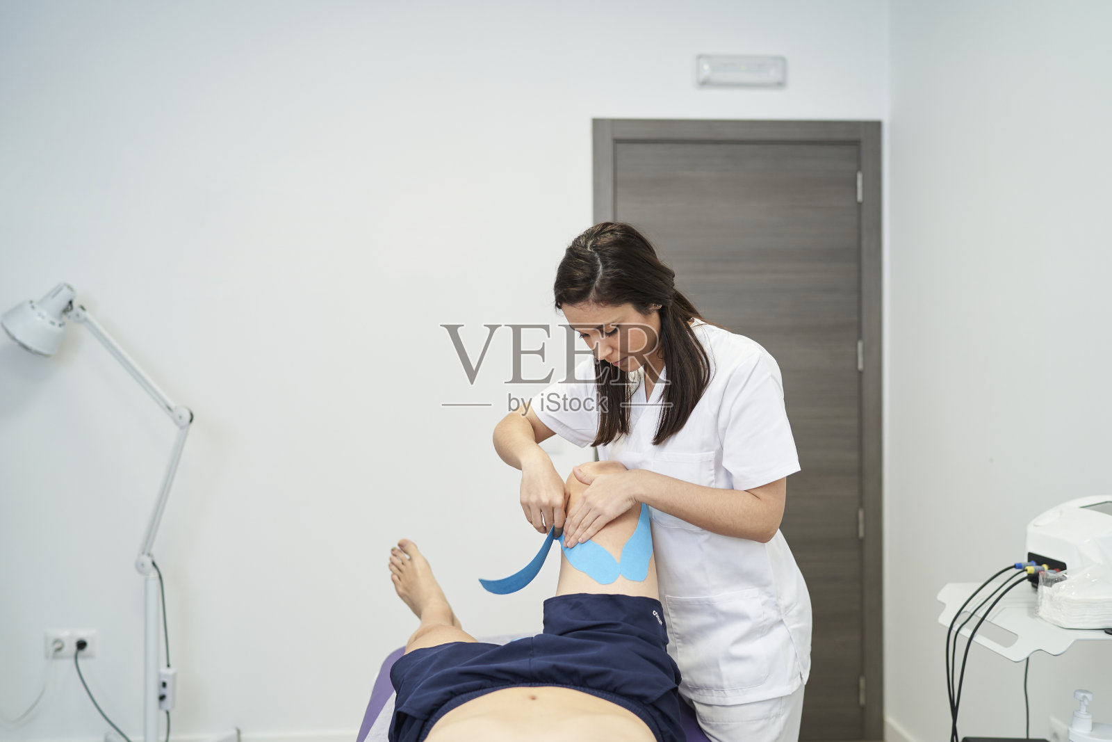 物理治疗师用神经肌肉胶布治疗病人的膝盖照片摄影图片