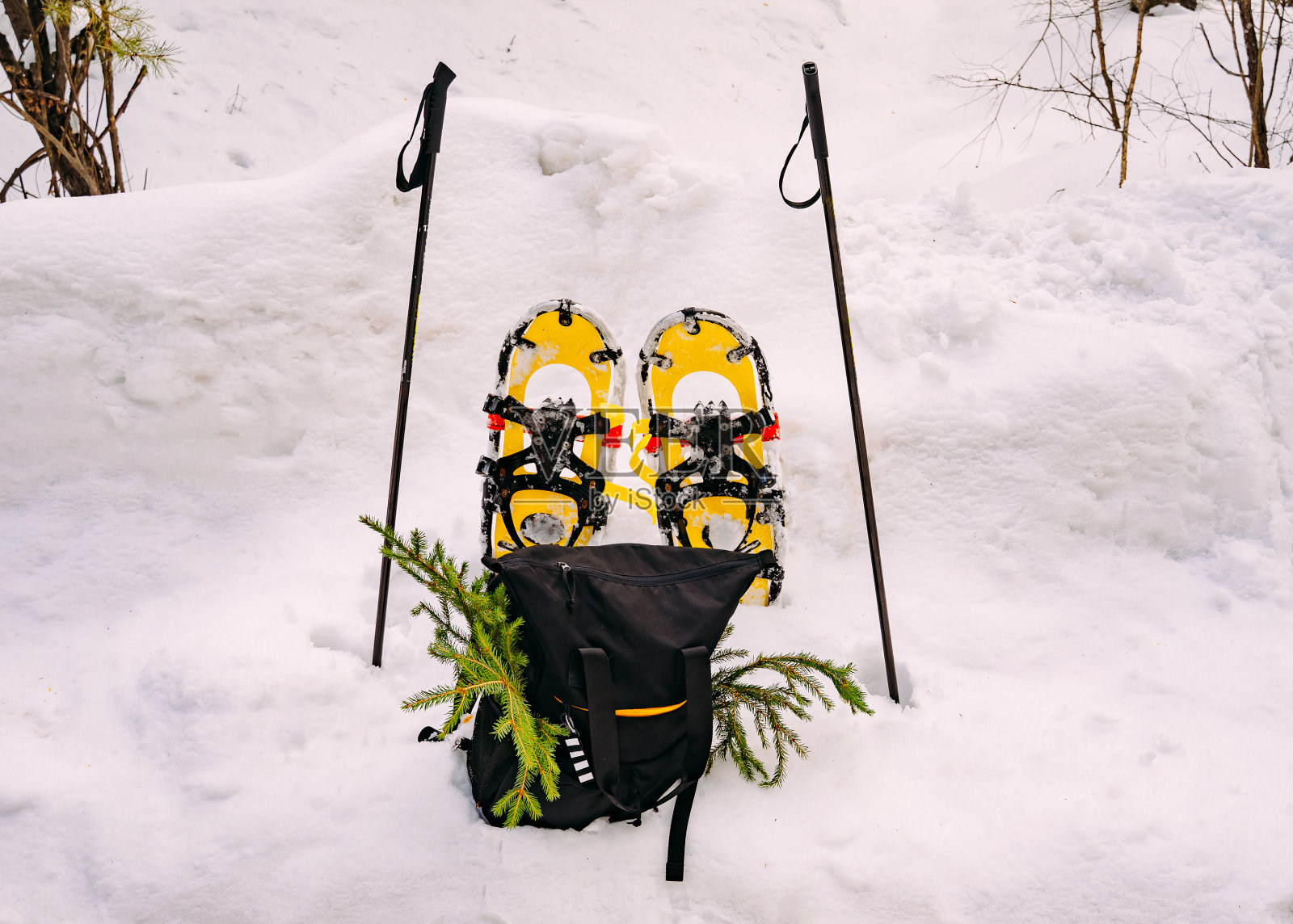 亮黄色的雪鞋在雪地里，旁边是登山杖和黑色的背包。冬天在树林里远足照片摄影图片