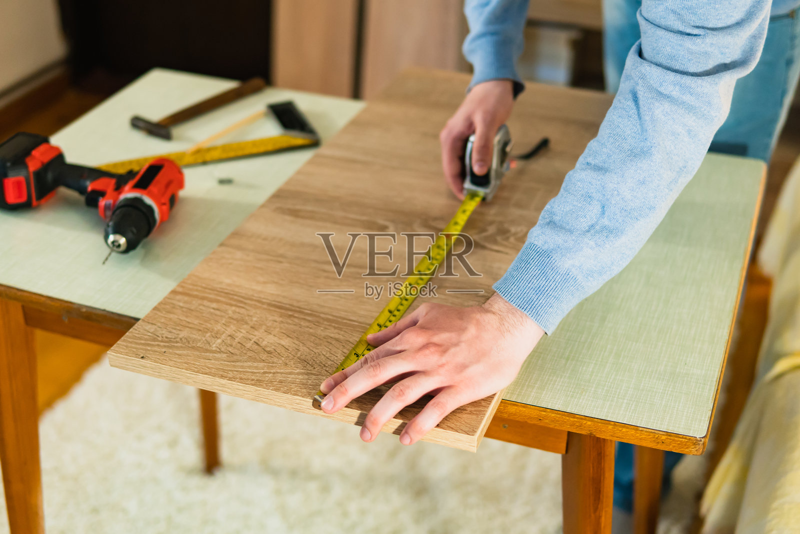 一个年轻人的手的特写，他用一个仪表标记他在家里做家具的木板(胶合板)。在家DIY项目。照片摄影图片