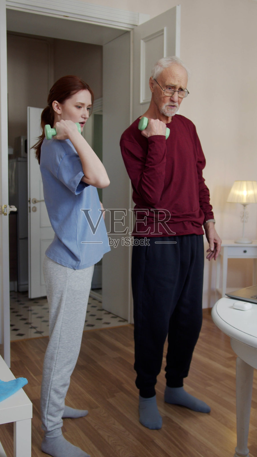 爷爷和教练一起举起哑铃。他们正在用笔记本电脑看健身视频照片摄影图片