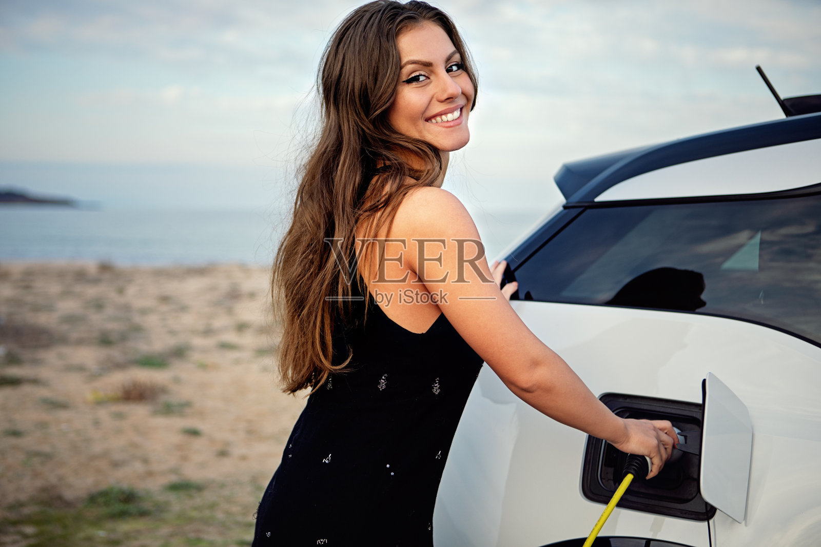 年轻女子在沙滩上给她的电动汽车充电的肖像照片摄影图片