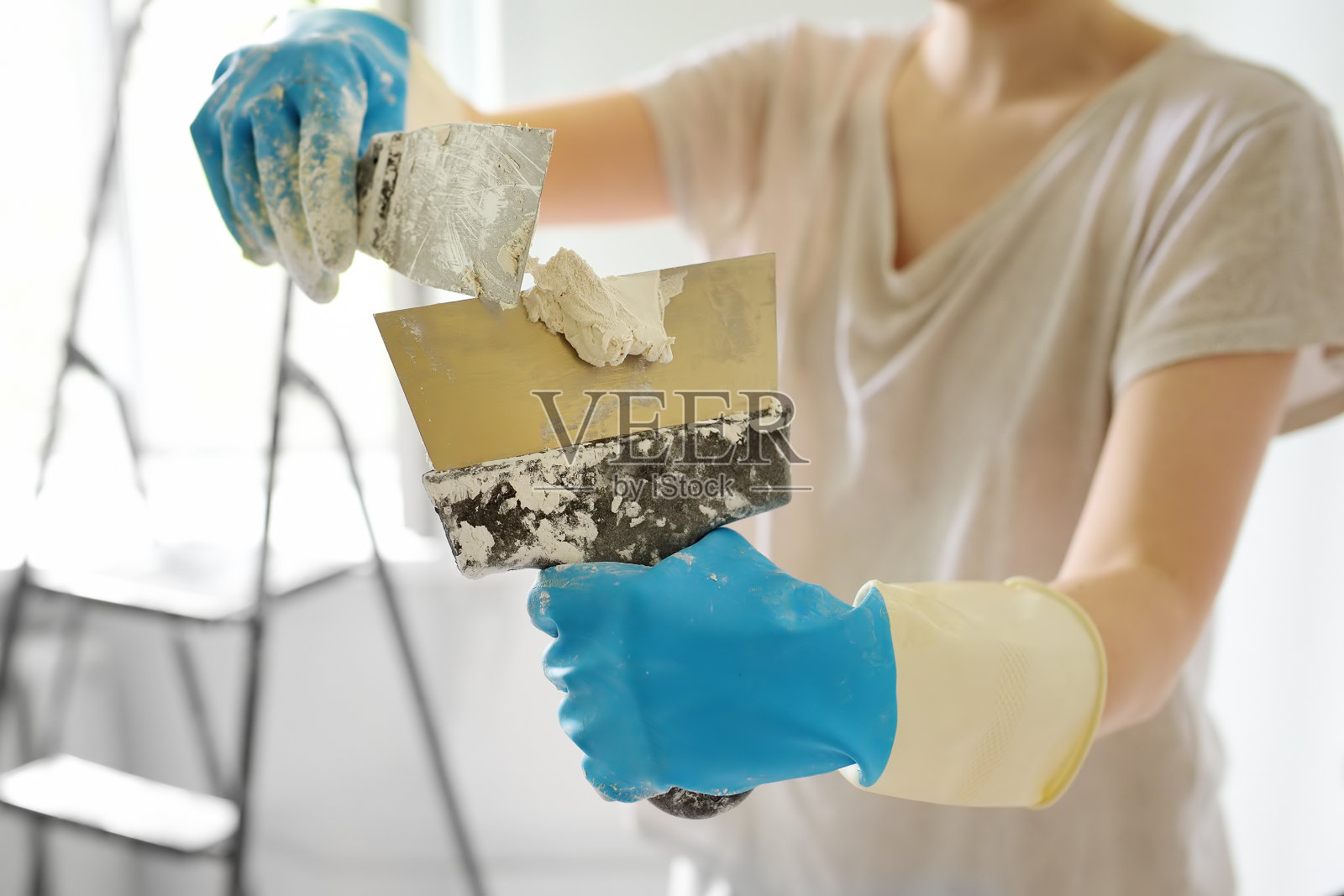 年轻的女工正在准备补墙用的油灰。在金属抹刀上涂抹石膏的特写。做你自己。照片摄影图片