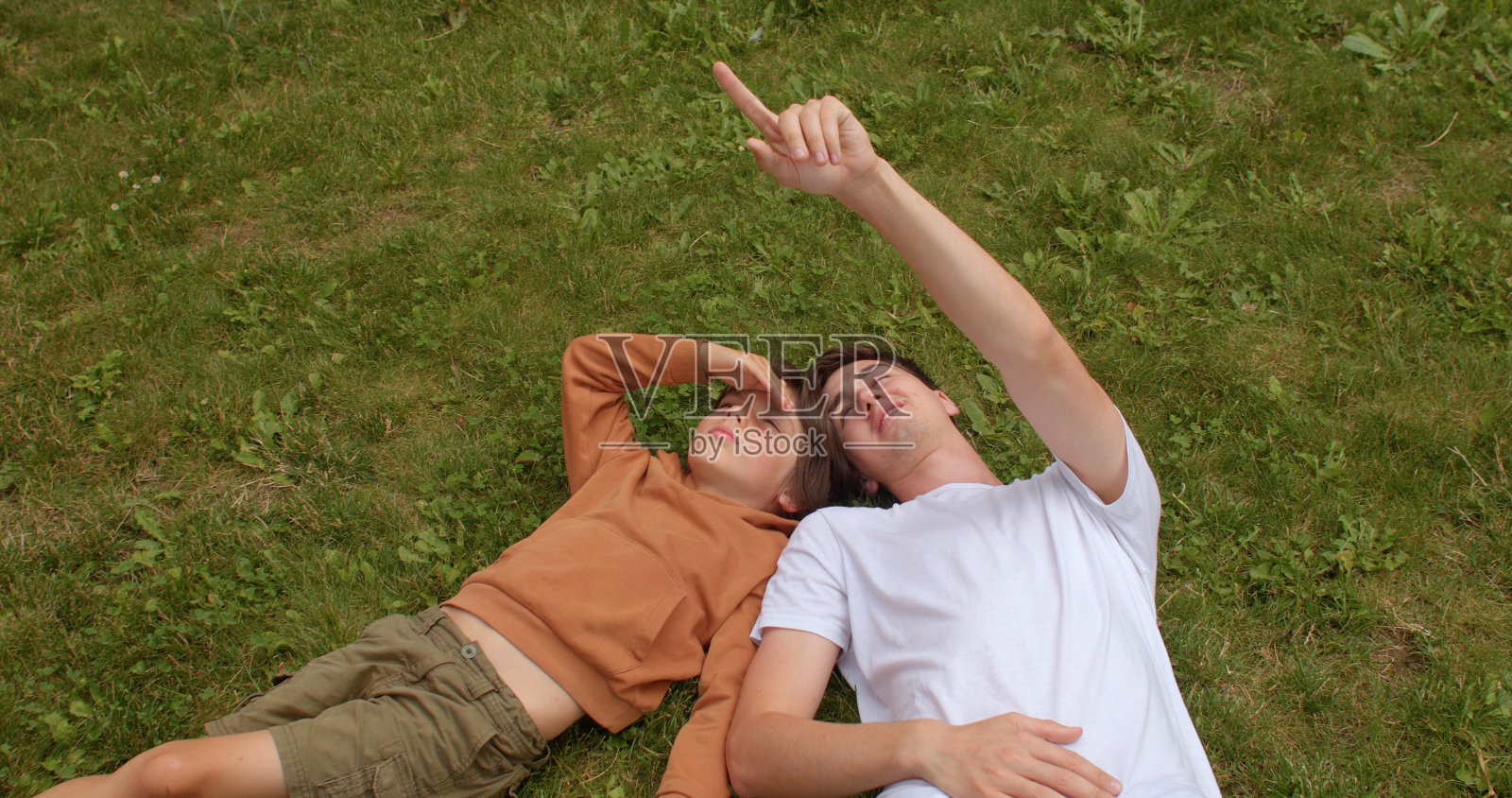 一个男孩和一个年轻人躺在草地上，看着天空。前视图。照片摄影图片