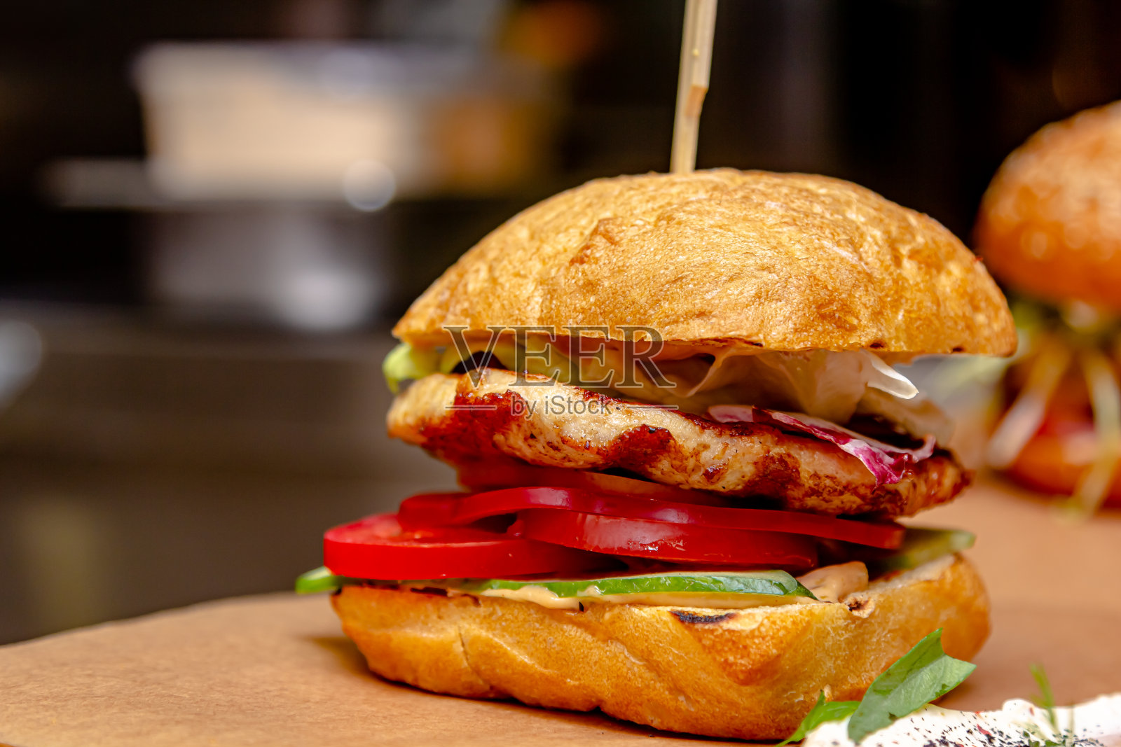 一块木板上放着一个汉堡，里面有炸鸡胸肉、西红柿和黄瓜照片摄影图片