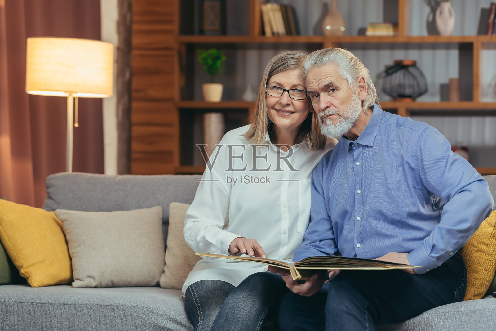 一对可爱的老夫妇坐在家里的沙发上看《回忆录》相册。年迈的祖父母坐在一起，看着和讨论着愉快的时刻，翻看着照片，怀旧之情油然而生照片摄影图片