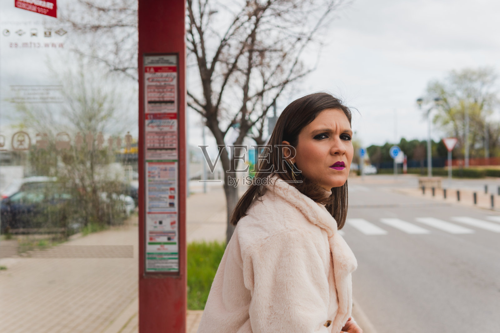 一个焦急的女人在公共汽车站等公共交通工具。照片摄影图片