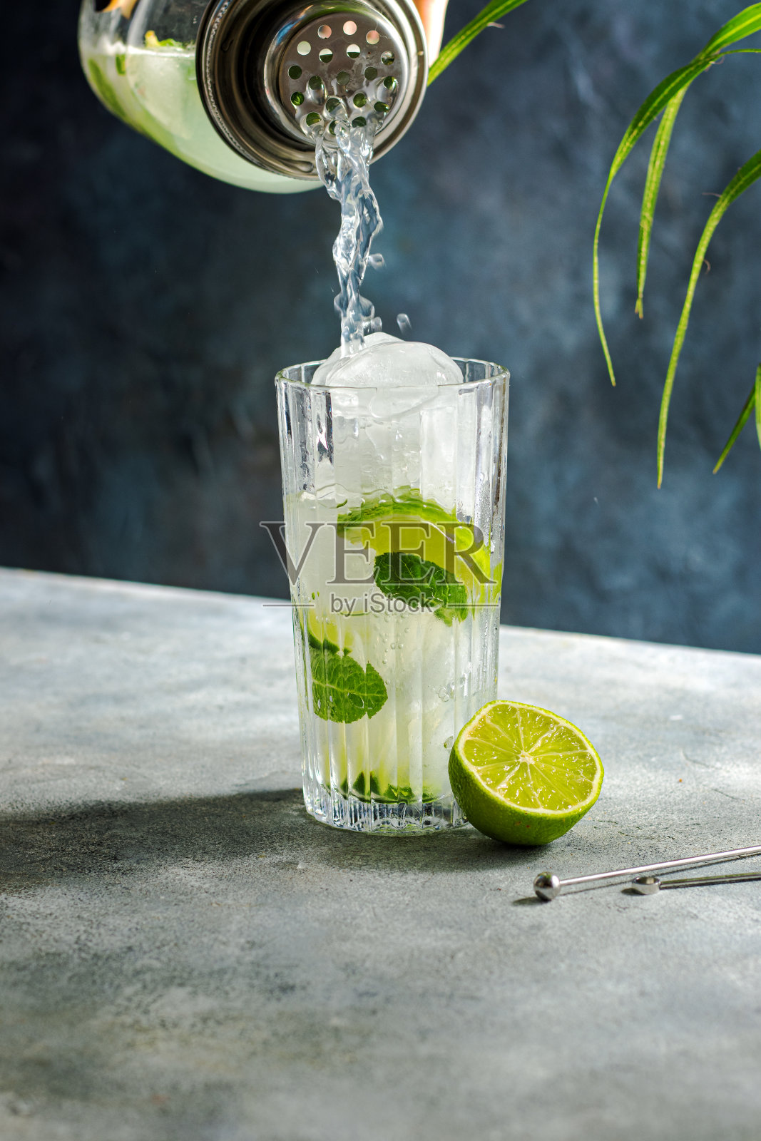 鸡尾酒的准备。一杯酸橙，冰块，薄荷。工具的鸡尾酒，酒吧招待调酒设备与莫吉托摇。往杯子里倒一杯鸡尾酒照片摄影图片