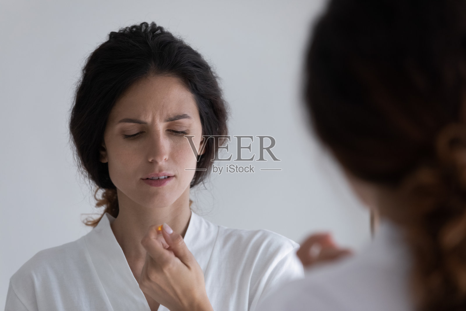 年轻不健康的皱眉头的女人，穿着浴袍，手里拿着药丸照片摄影图片