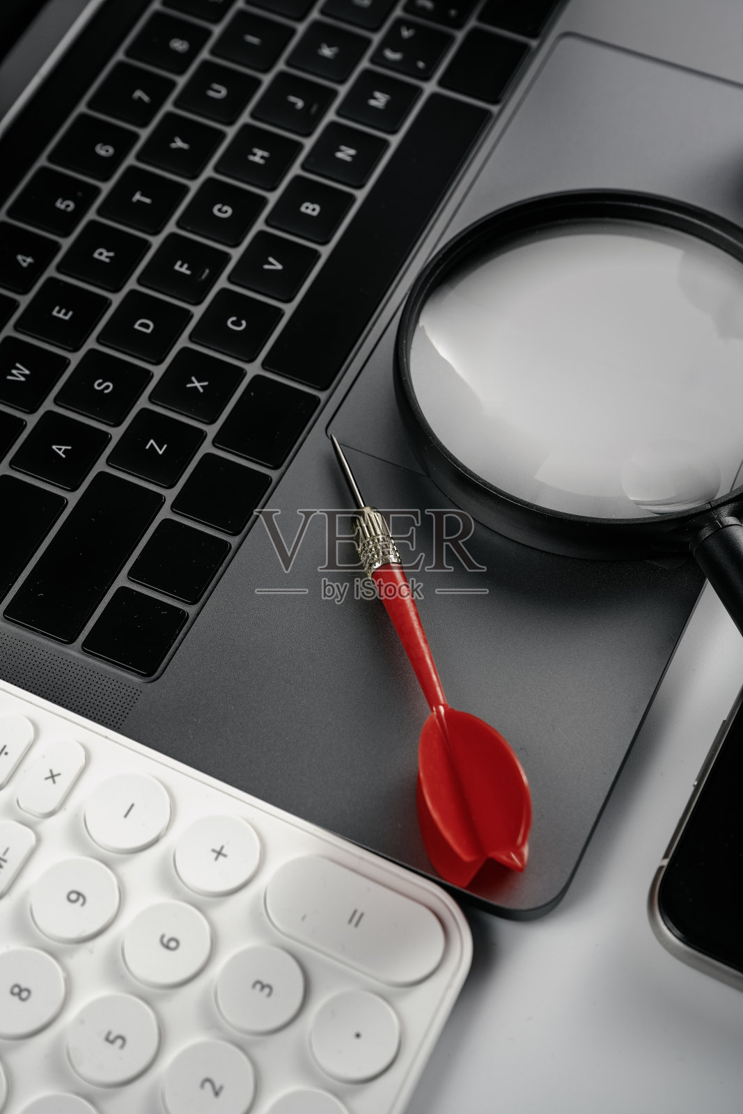 电脑在白色背景板，放大镜，飞镖，耳机和计算器照片摄影图片