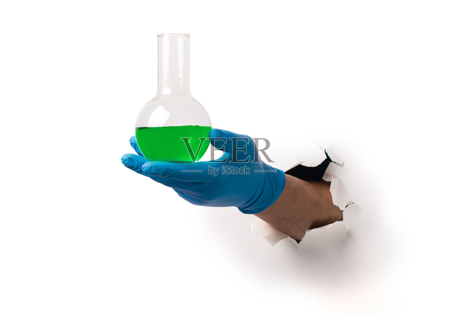 从白纸上的一个破洞里拿着绿色液体的玻璃瓶子。照片摄影图片