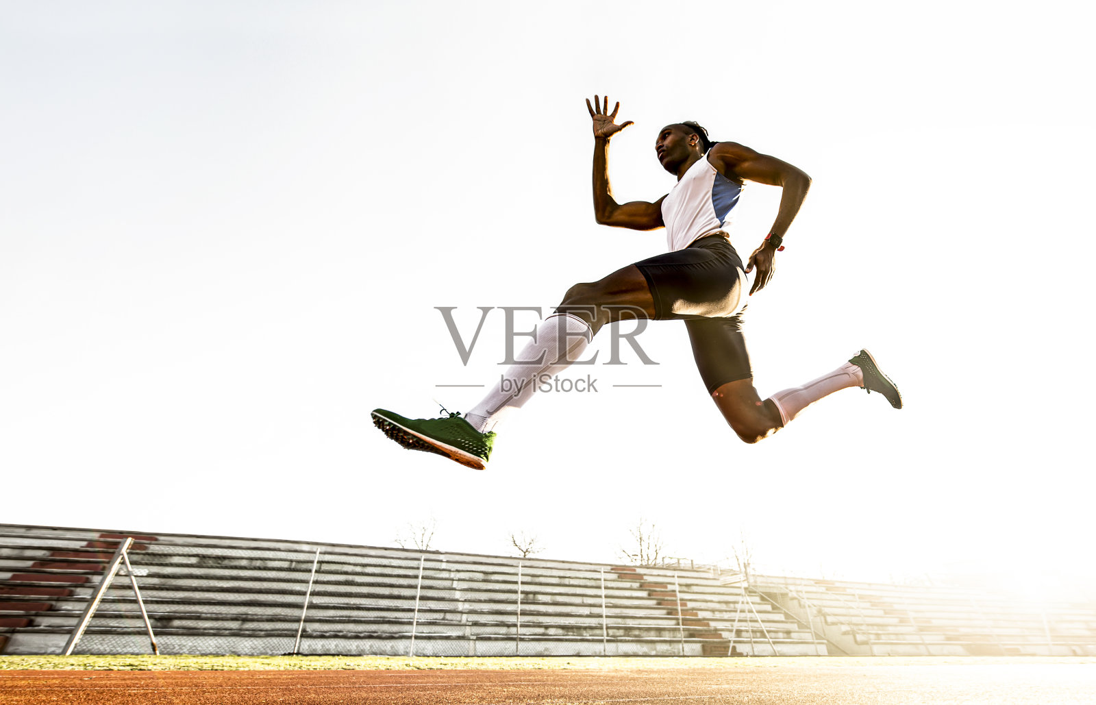 职业非洲裔美国男子田径运动员在障碍赛跑-年轻运动员表演爆发性跳远训练在跑道上在田径体育场-自由的概念照片摄影图片