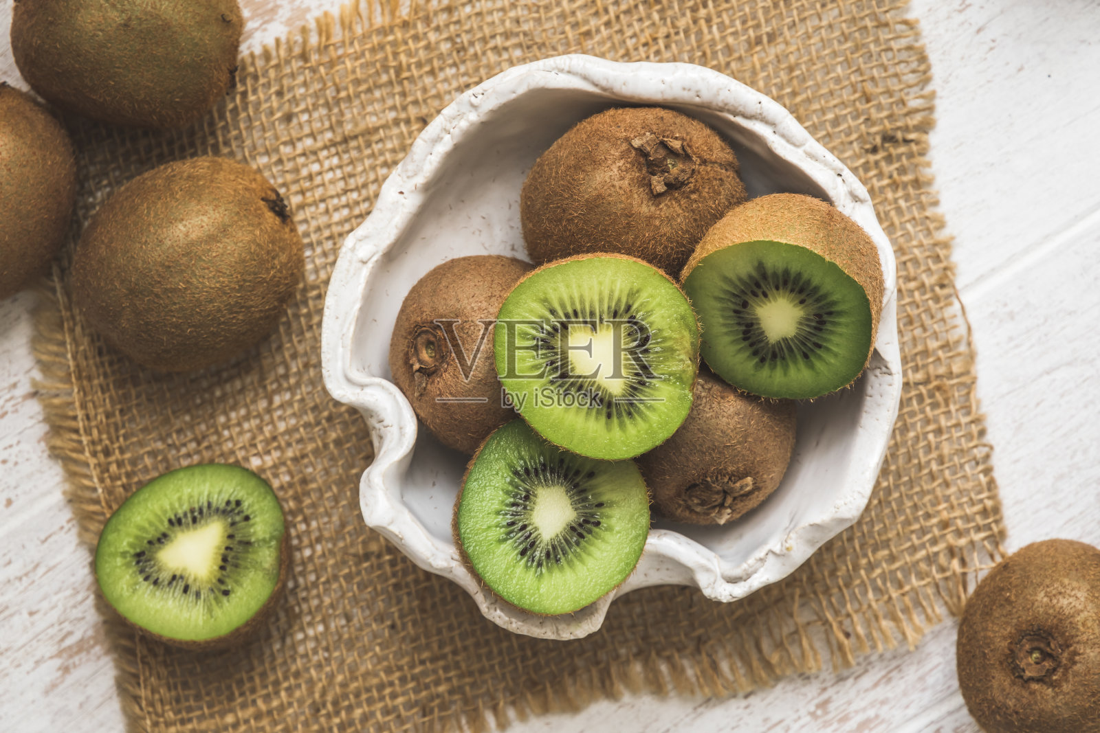 白色木桌上，碗里放着整只和半只猕猴桃照片摄影图片