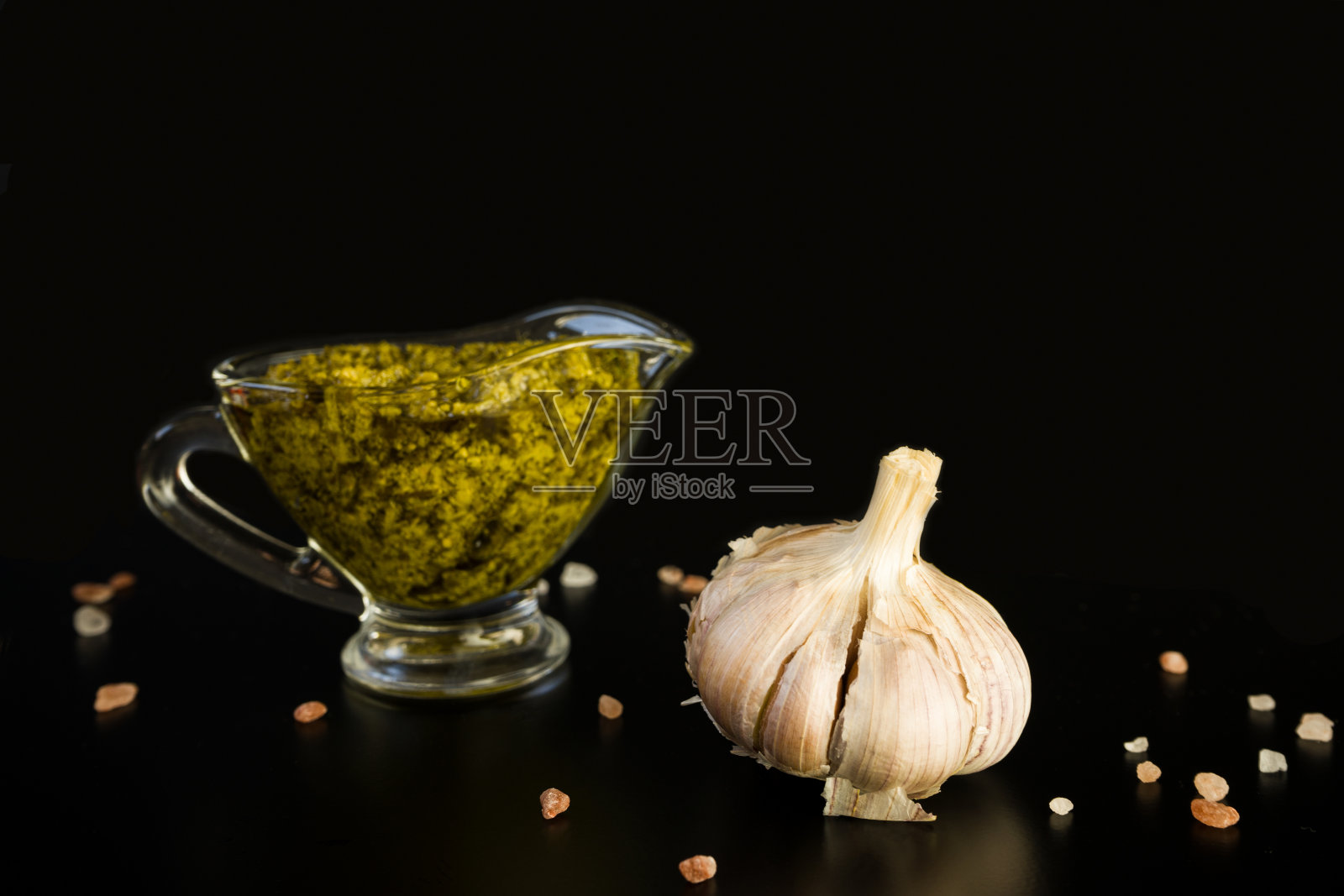 意大利香蒜沙司装在玻璃平底锅里，蒜头和玫瑰盐在黑色的背景上。照片摄影图片