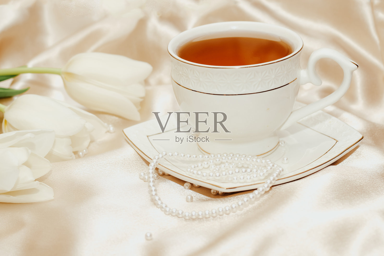 白色郁金香花束与珍珠珠和茶在丝绸金色裸缎背景照片摄影图片