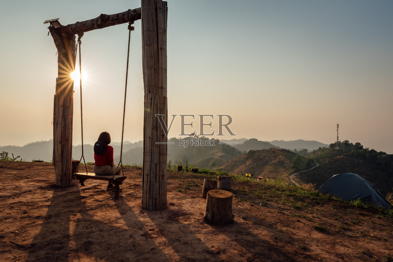 孤独的女人坐在秋千上，看着夕阳西下的时候。照片摄影图片