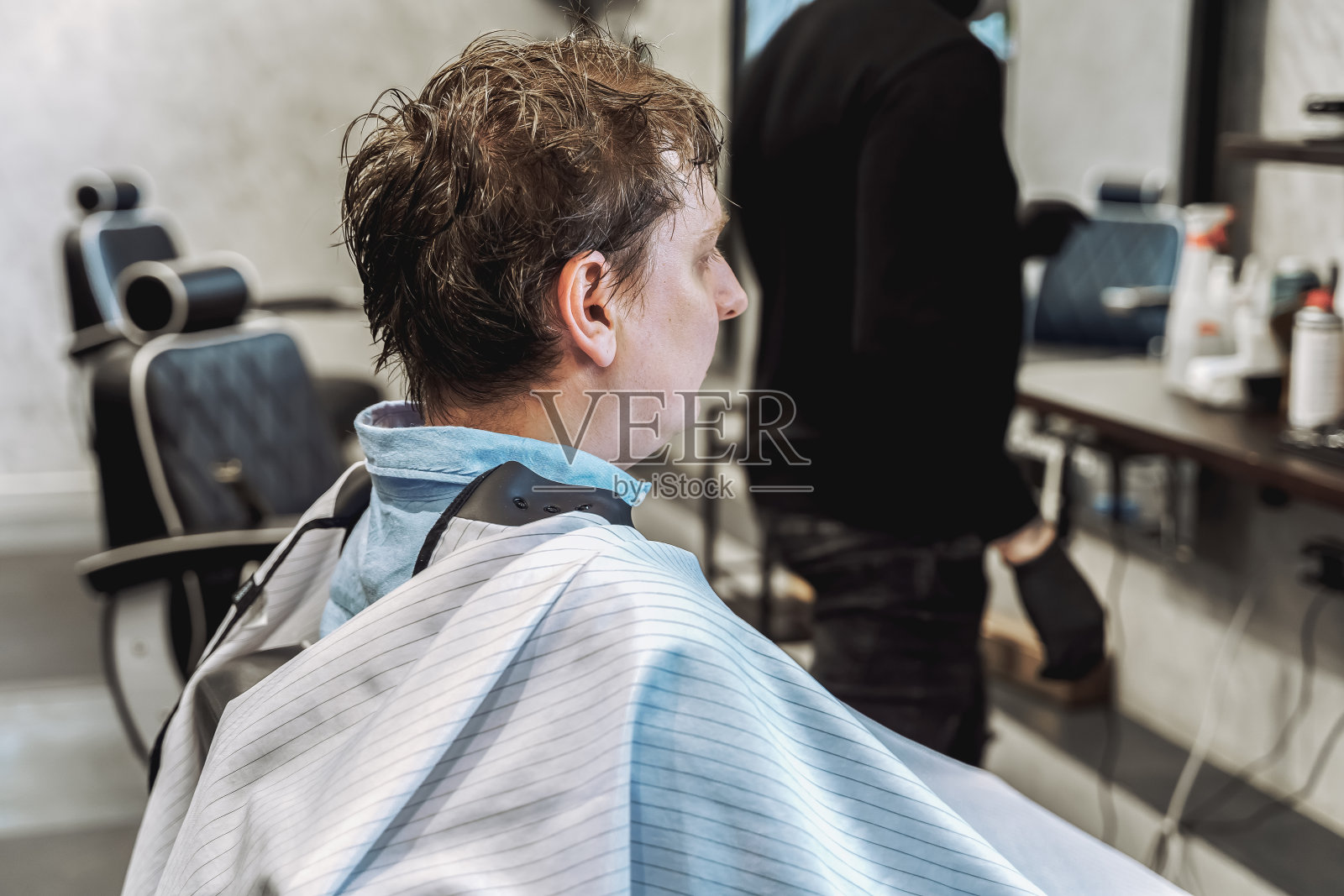 去理发店。年轻时尚的男人，商人做时尚的发型。理发师，发型师，造型师和客户，顾客坐在黑暗的男子美容沙龙黑色的椅子盖着一个披肩照片摄影图片