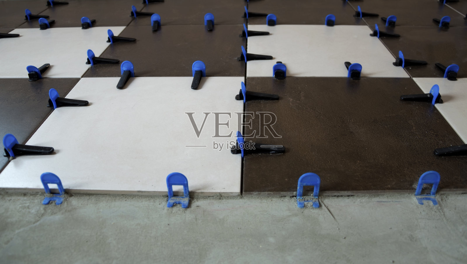 使用夹子和楔子在地板上铺设瓷砖。照片摄影图片