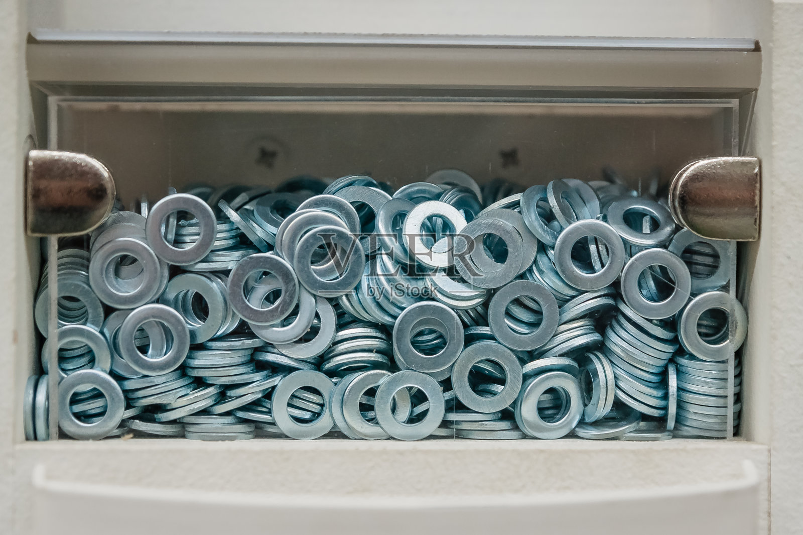一个透明盒子里装了很多金属垫圈。将紧固件和零件存放在一个单元中照片摄影图片