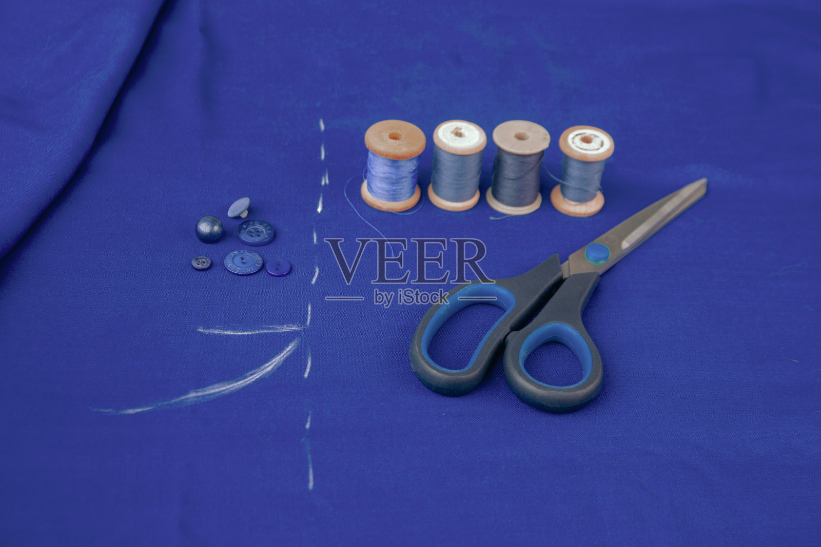 有粉笔记号的蓝色布料，剪刀，线，纽扣。织物的质地。照片摄影图片