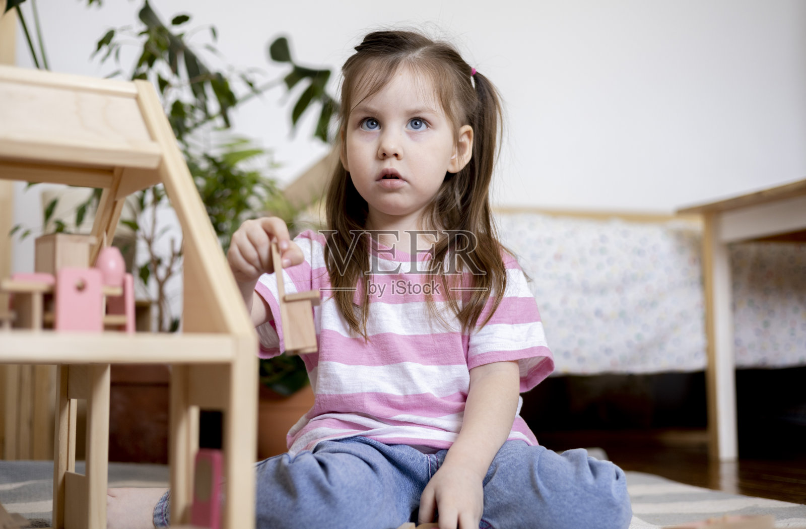 蒙特梭利的材料。一个穿着粉色t恤的小女孩在玩偶屋里整理木制家具。照片摄影图片