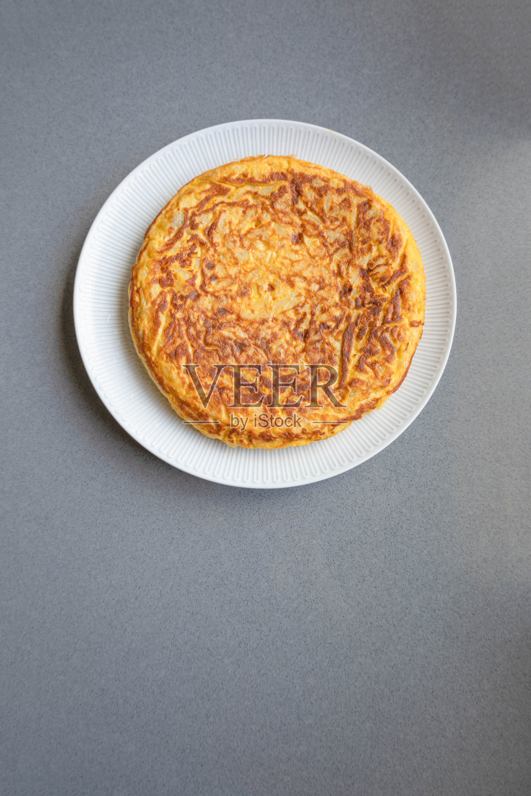 西班牙煎蛋卷，有土豆和洋葱，在一个白色的盘子里，有很多灰色的负空间来抄写照片摄影图片