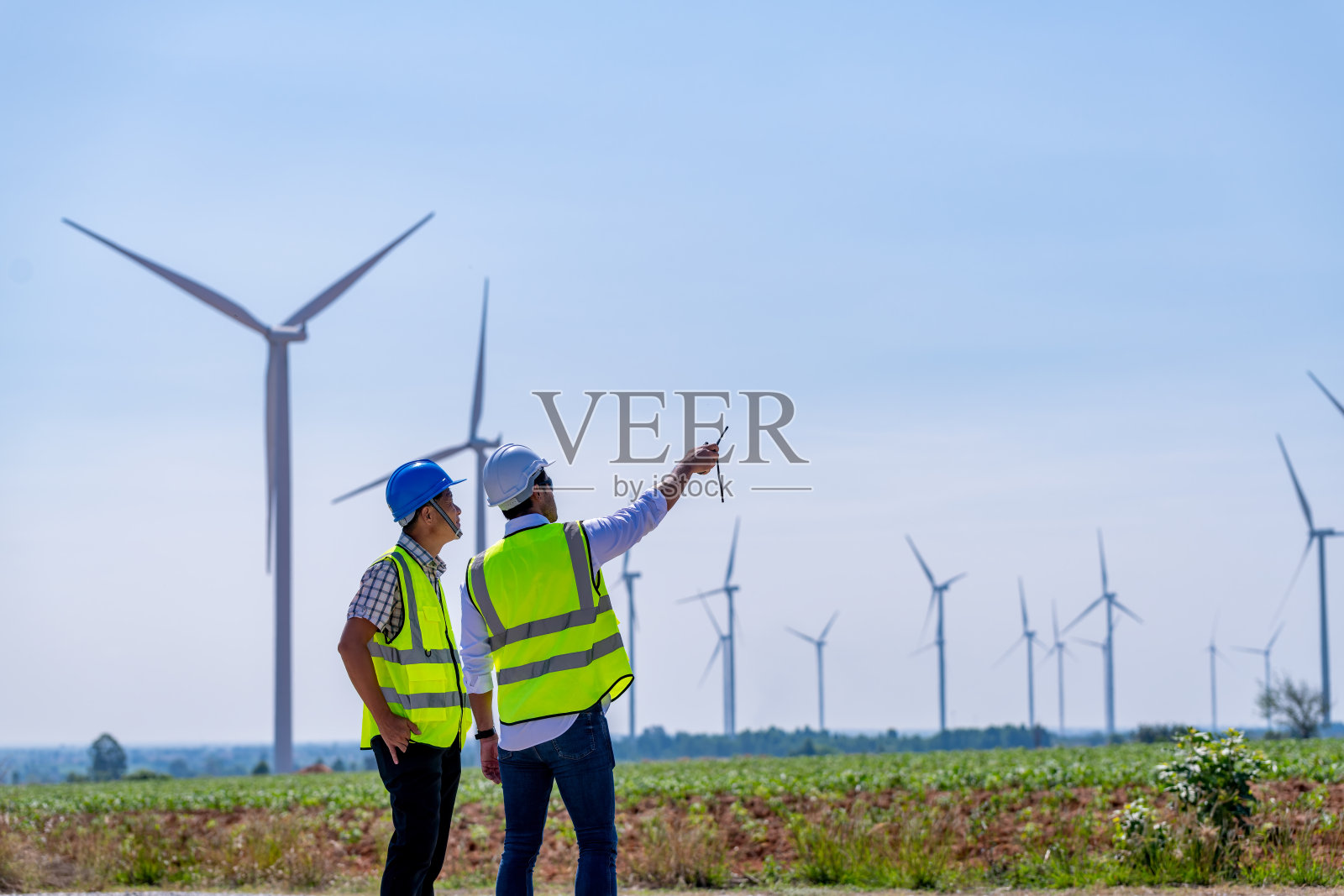 工程师穿着制服，戴着头盔持文件检查工作，在风电场旋转发电。绿色生态发电、风力发电、可持续能源理念。照片摄影图片