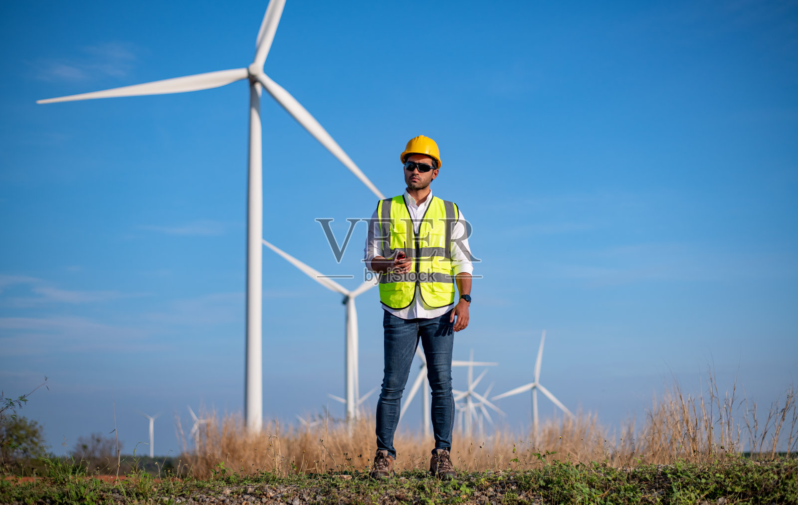 工程师穿着制服，戴着头盔持文件检查工作，在风电场旋转发电。绿色生态发电、风力发电、可持续能源理念。照片摄影图片
