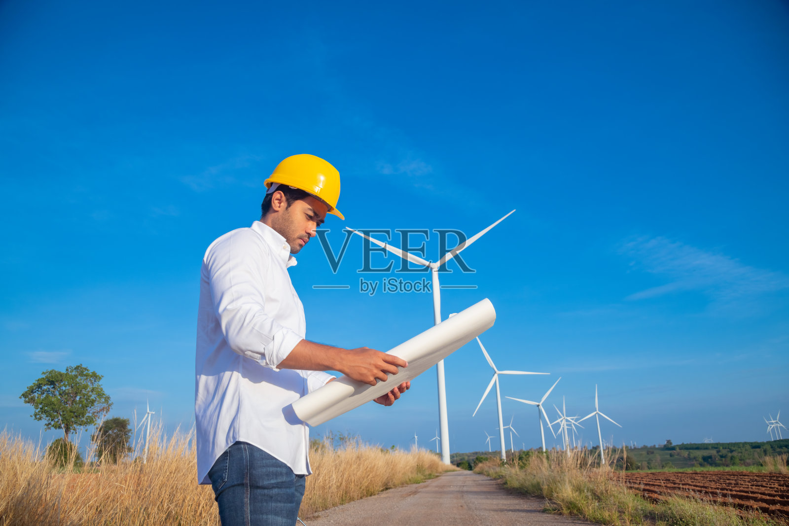 工程师穿着制服，戴着头盔持文件检查工作，在风电场旋转发电。绿色生态发电、风力发电、可持续能源理念。照片摄影图片