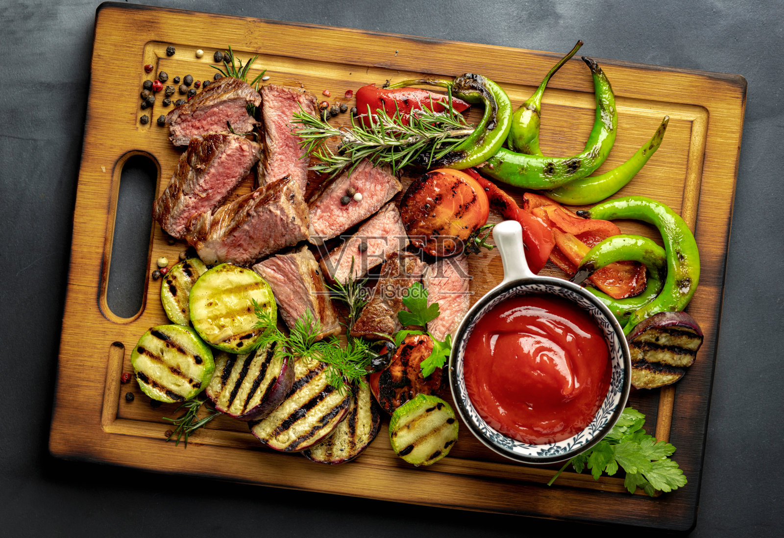 切片煎中牛排与烤蔬菜和番茄酱酱木砧板上深色背景特写俯视图照片摄影图片