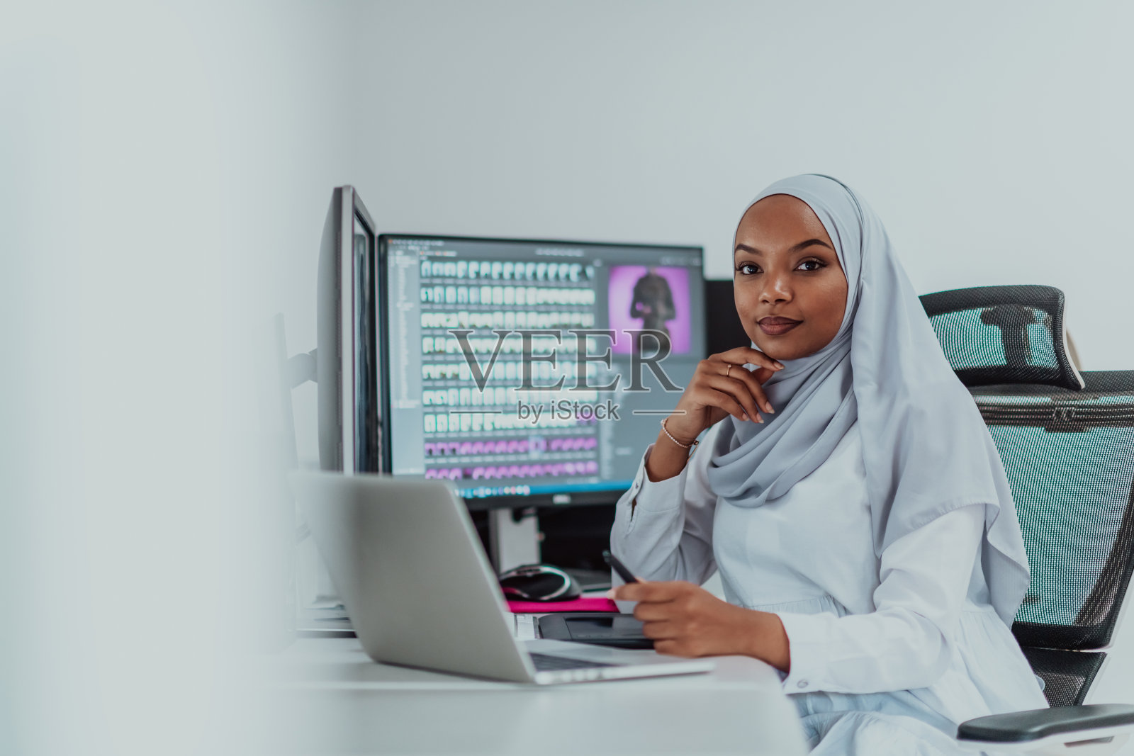 年轻的非裔美国现代穆斯林女商人戴着围巾，在一个有大屏幕的创造性明亮的办公室工作场所照片摄影图片