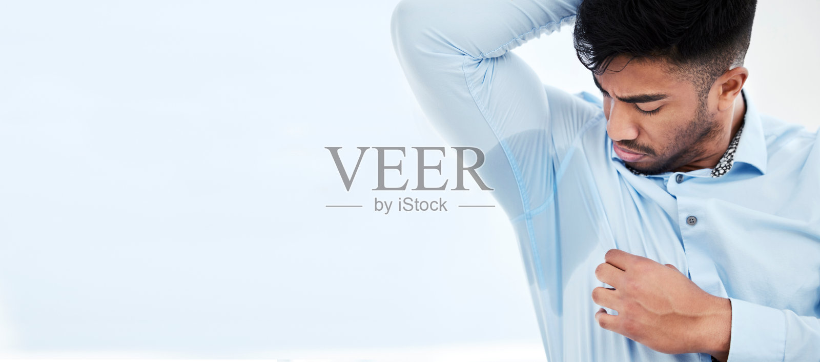 拍摄的是一名年轻的商人，汗渍浸透了衬衫的腋下照片摄影图片