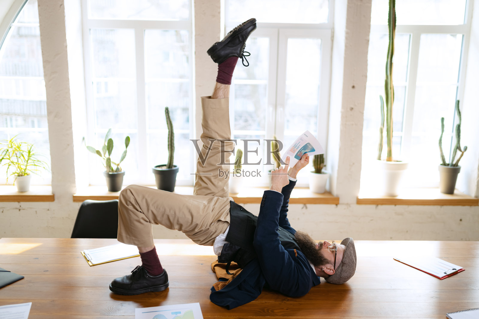 年轻的大胡子，办公室职员，在现代办公室的工作时间，在木桌上用电子设备做瑜伽。商业理念，健康生活方式，运动，爱好照片摄影图片