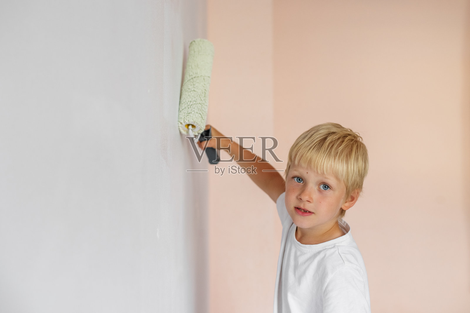 家庭装修。小男孩用油漆滚筒刷内墙照片摄影图片