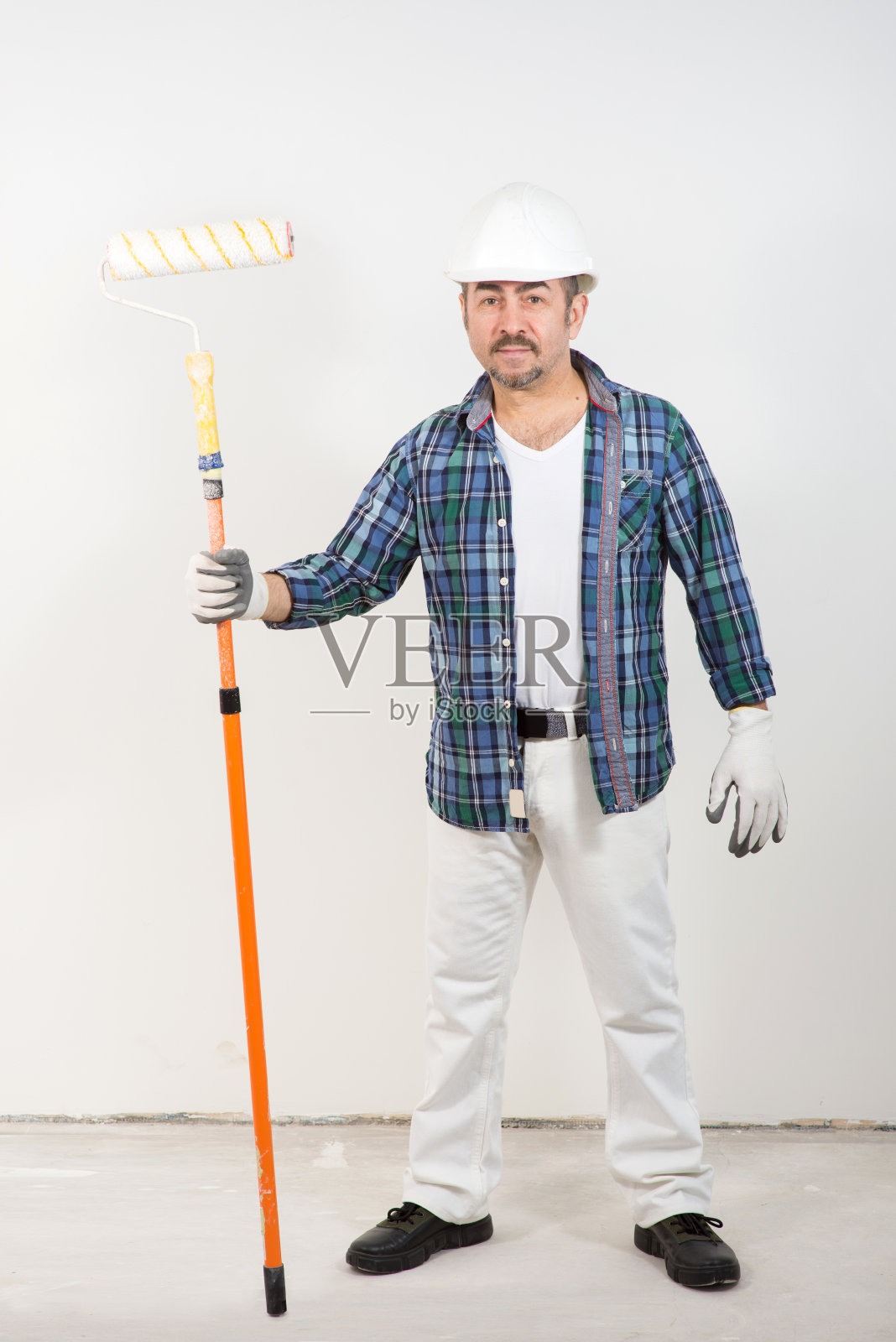 建筑工修理工手里拿着一个长长的油漆滚筒，背景是白色的墙壁照片摄影图片