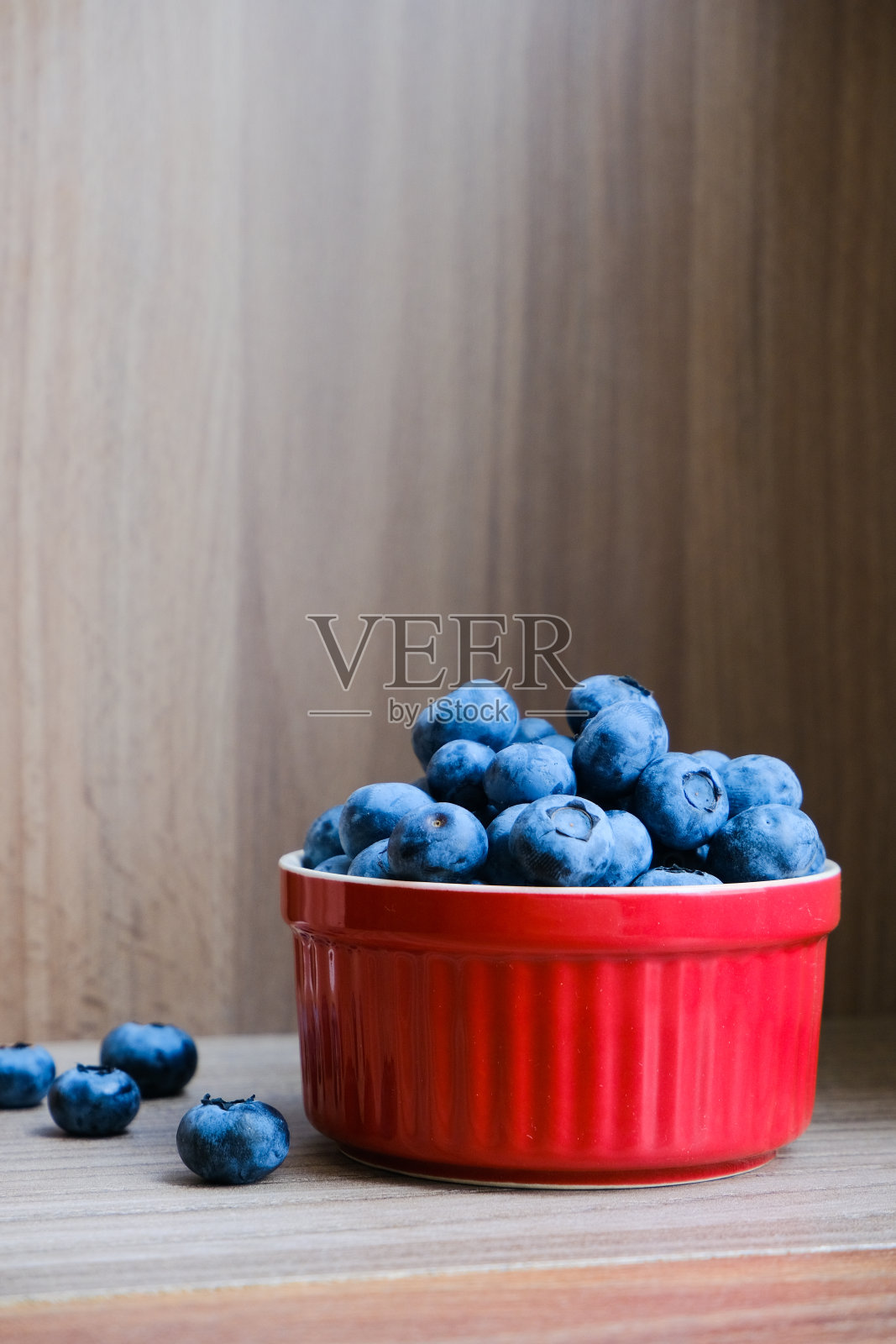 木桌上的红色盘子里盛着新鲜的有机蓝莓。健康的营养。照片摄影图片