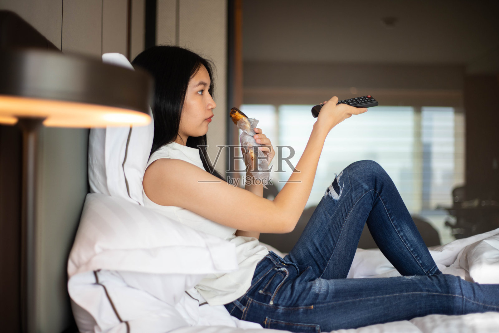 女人一边吃零食一边按电视遥控器照片摄影图片