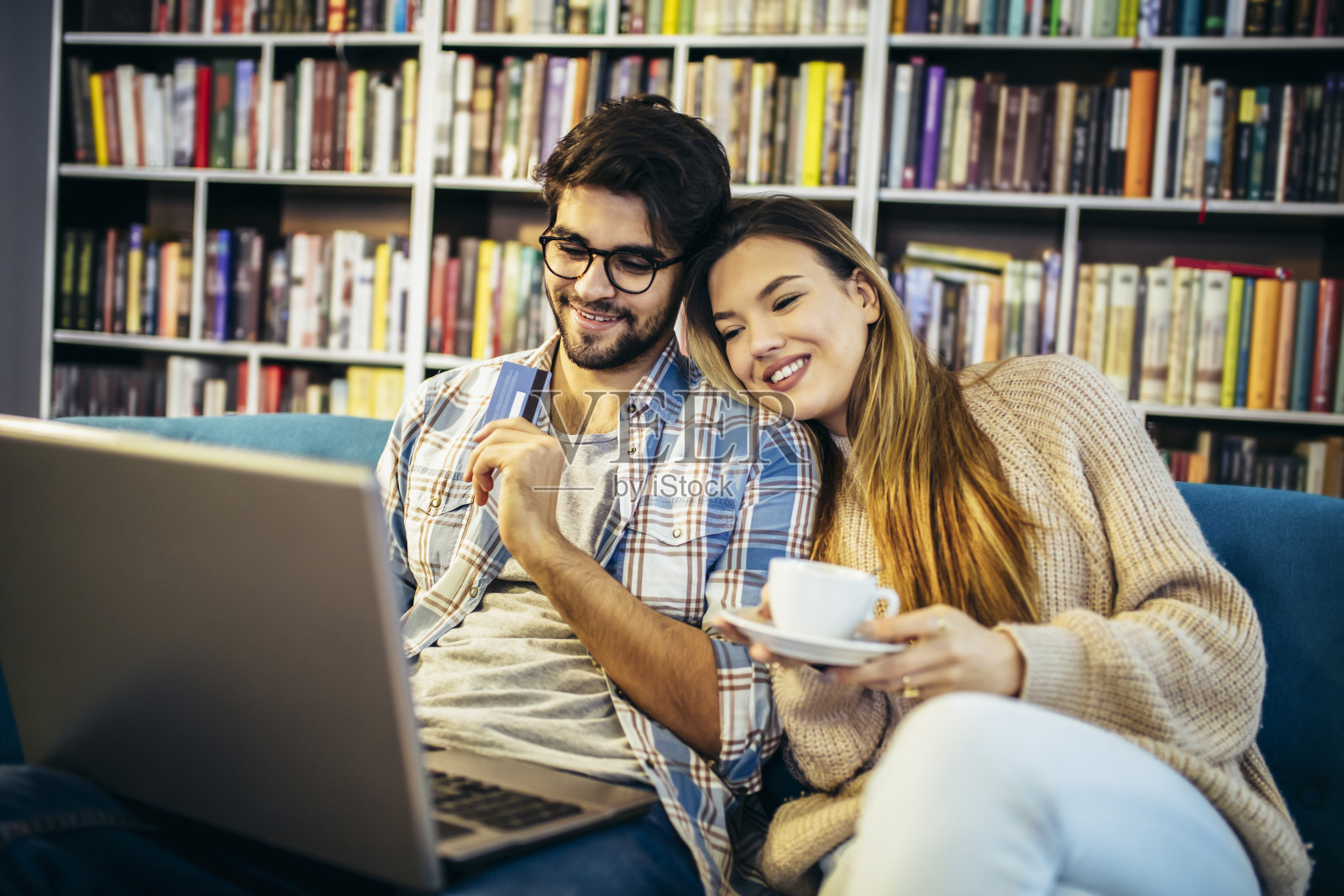 漂亮的年轻夫妇带着笔记本电脑在咖啡馆，他们用信用卡在网上购物。照片摄影图片