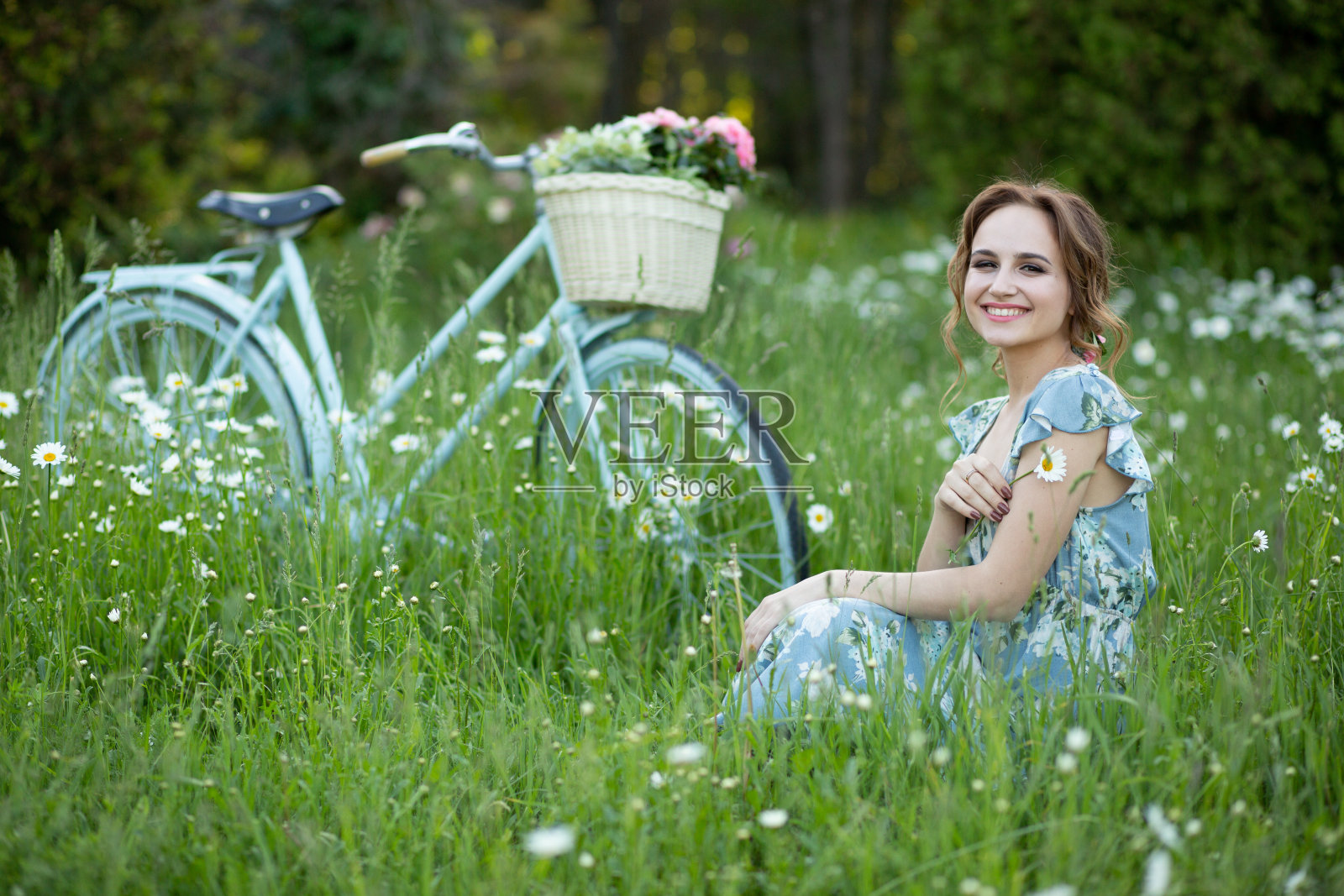 画像上一个美丽的女孩在森林里，抱着自行车，提着花篮，在阳光的照射下，穿着蓝色的花裙，夏日漫步照片摄影图片