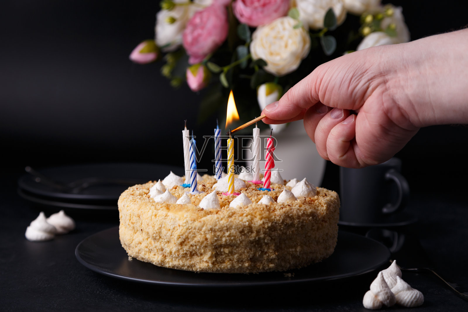 整个生日蛋糕加上脆酥饼屑和迷你蛋白霜。一个男人在蛋糕上点燃蜡烛。点燃的生日蛋糕照片摄影图片