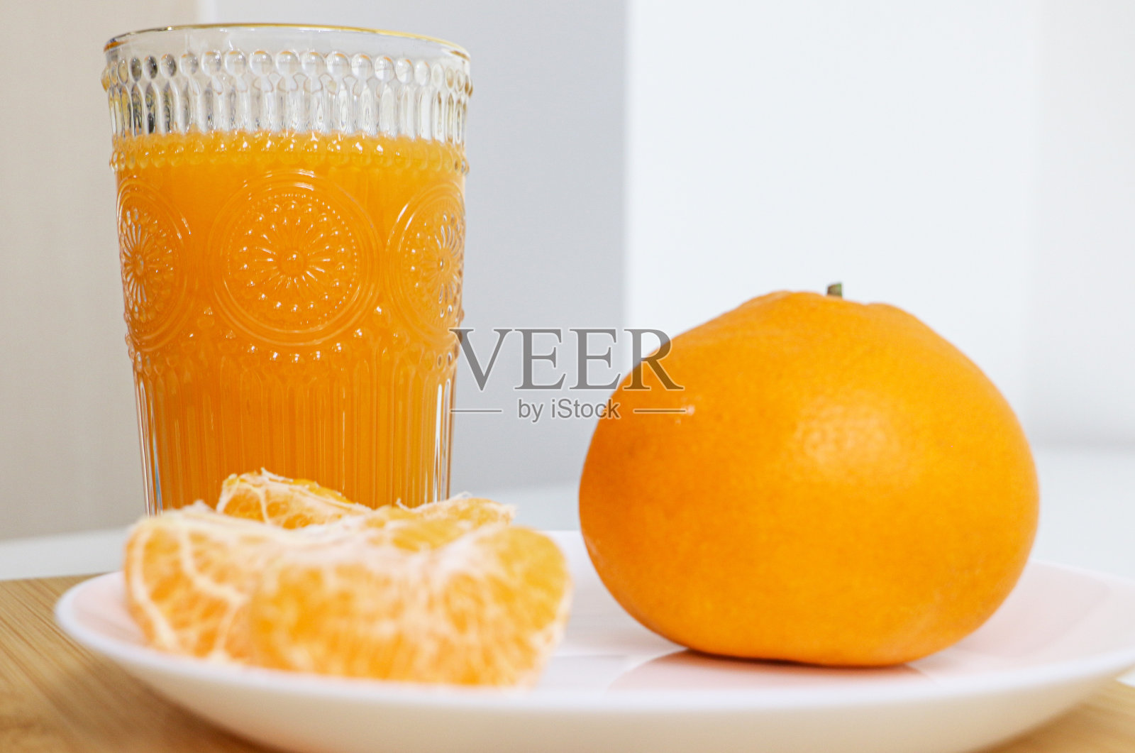 一杯天然桔子汁在背景的焦点，一个完整的圆形桔子和剥了皮的桔子片在盘子在前景的焦点外，选择性的焦点使用照片摄影图片